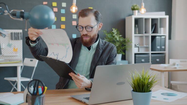Owner reviewing financial charts and a laptop at a desk.